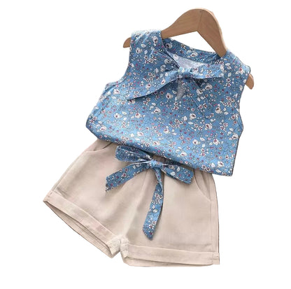 Children's outfit with floral top and beige shorts on a wooden surface.