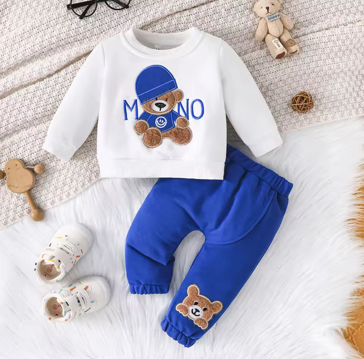 Children's outfit with white shirt and blue pants featuring teddy bear graphics on a textured surface.