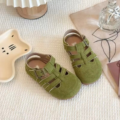 Green children's sandals on a textured surface with a star-shaped object and bottle in the background.