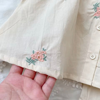 Close-up of a beige shirt with floral embroidery held by a hand.