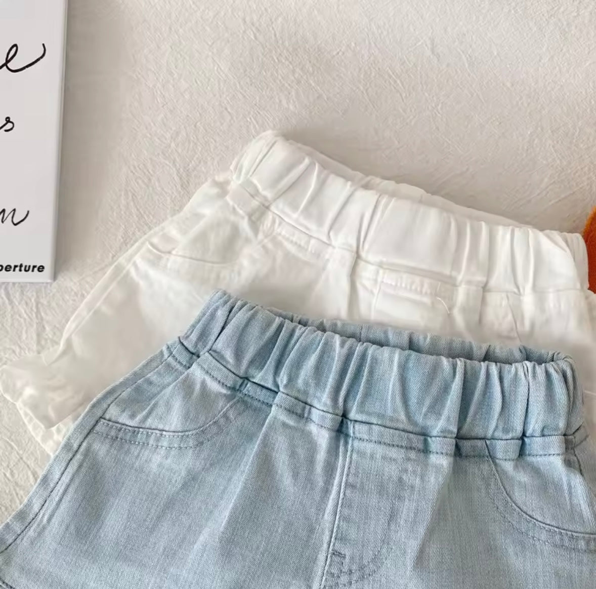 Light blue denim shorts and white top on a light gray surface with a blurred background.