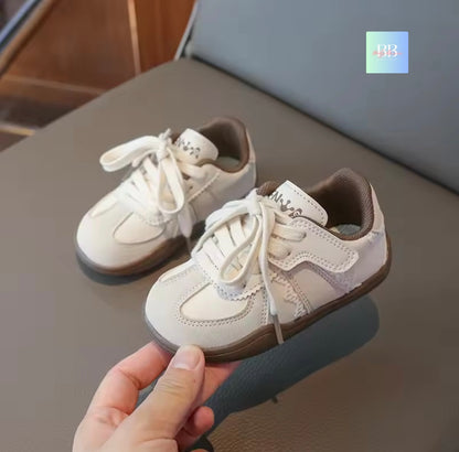 Pair of white sneakers with brown soles held by a hand on a reflective surface.