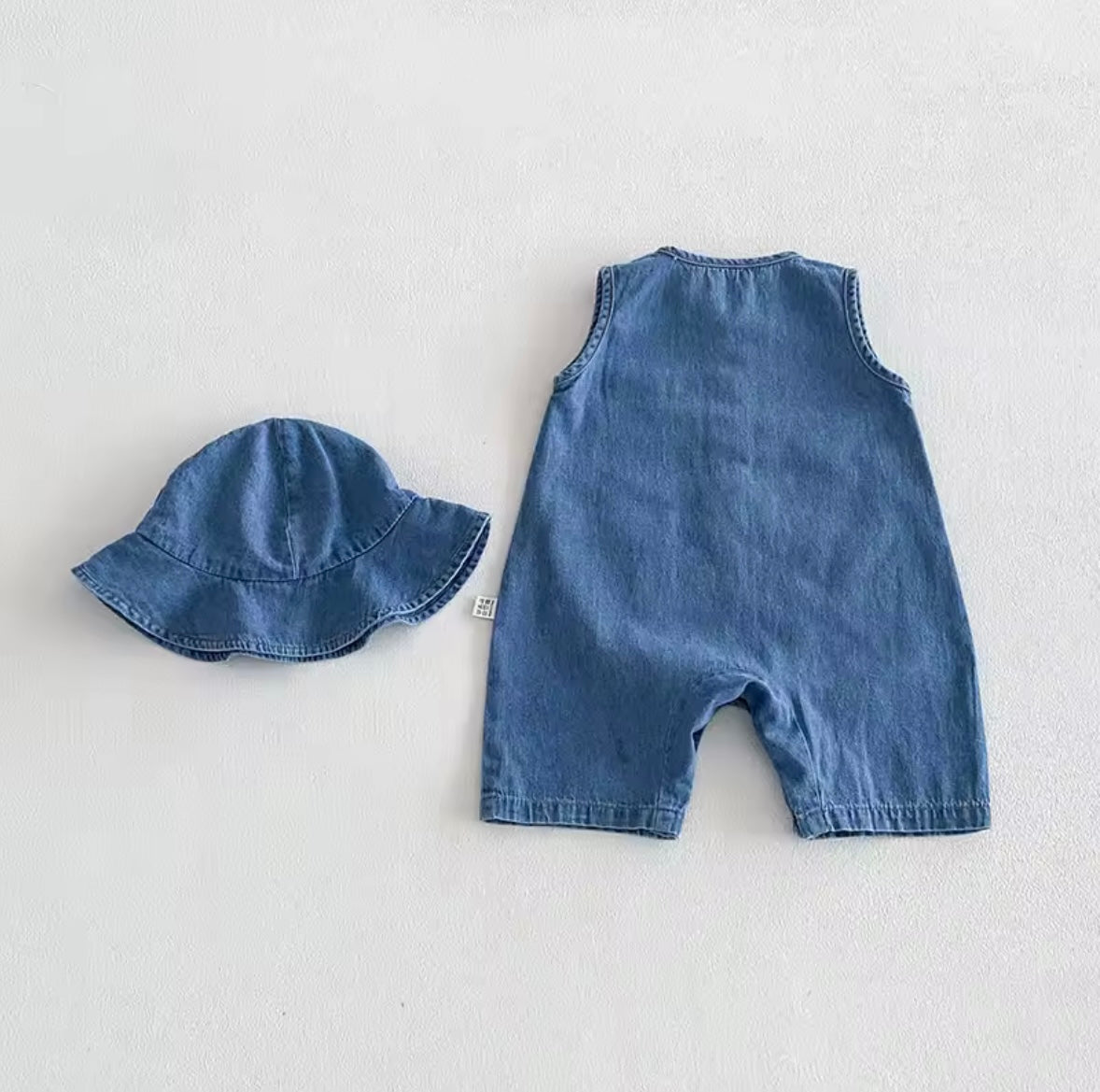 Blue denim romper and hat set on a light gray background