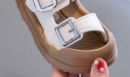 Brown sandal with white strap held by a hand with floral nail design.