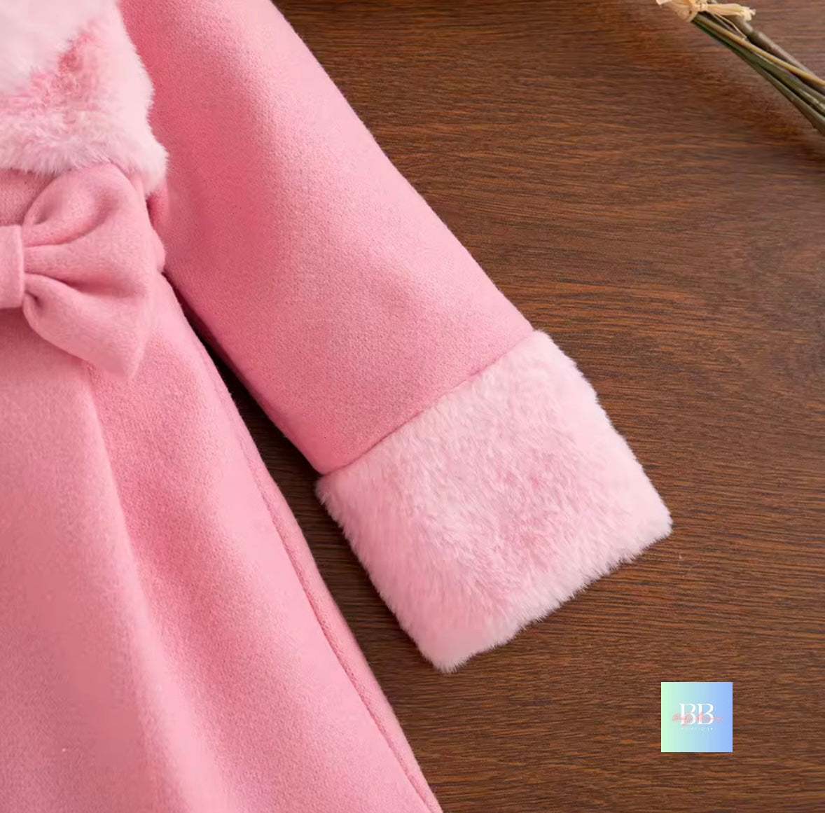 Close-up of a pink coat with a bow on a wooden surface