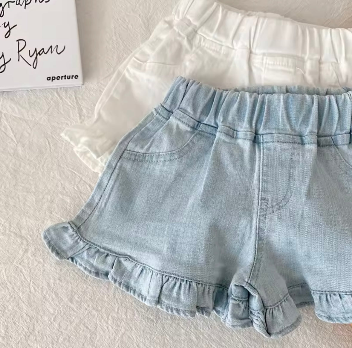 Light blue denim shorts with ruffled hem on a textured surface
