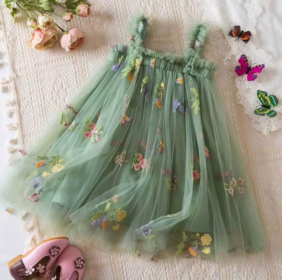 Green embroidered dress on a textured surface with flowers and butterflies.