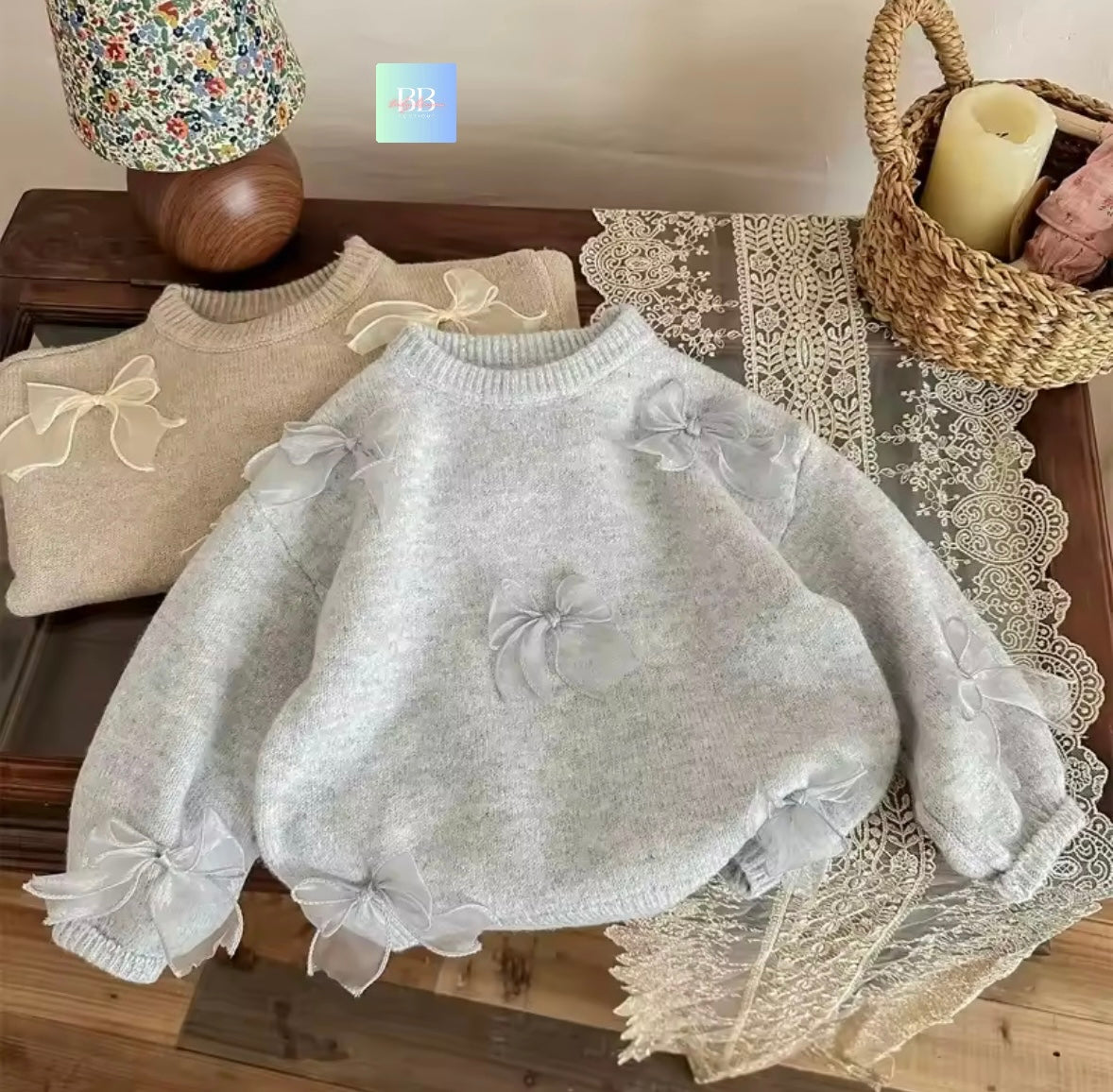 Light gray sweater with bow details on a lace tablecloth