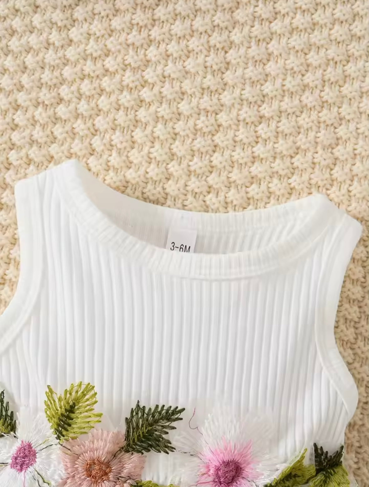 White sleeveless top with floral and leaf patterns on a textured beige background