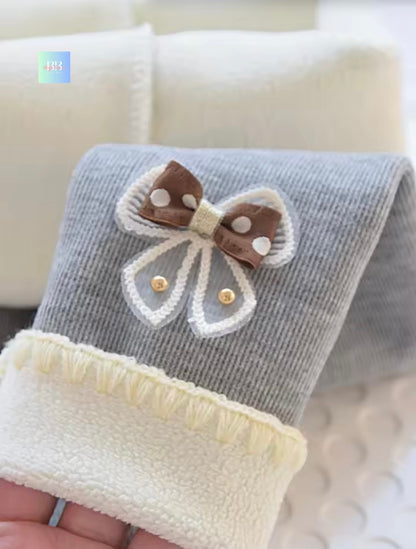 Gray baby booties with a brown and white bow held by a hand on a light background