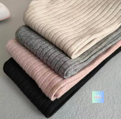 Stack of folded ribbed knit fabrics in black, pink, gray, and beige on a neutral background.