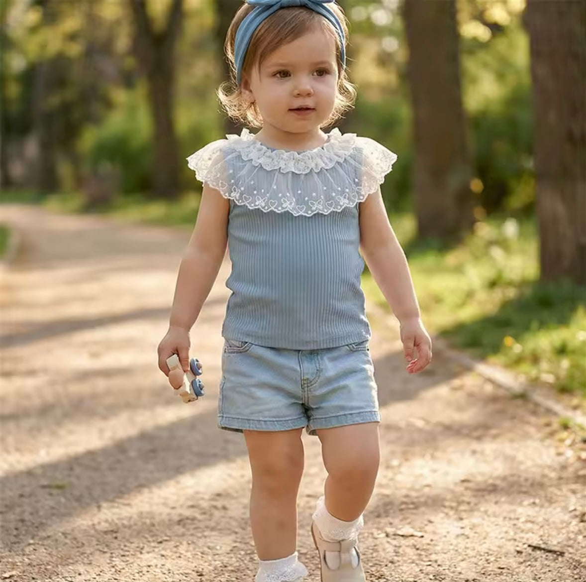 Child in a blue outfit with ruffled collar walking on a path outdoors