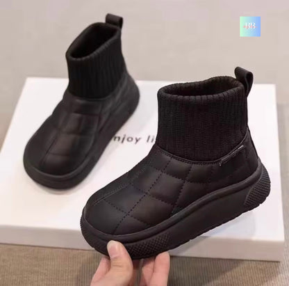 Black quilted ankle boots on a white box with a hand holding one boot.