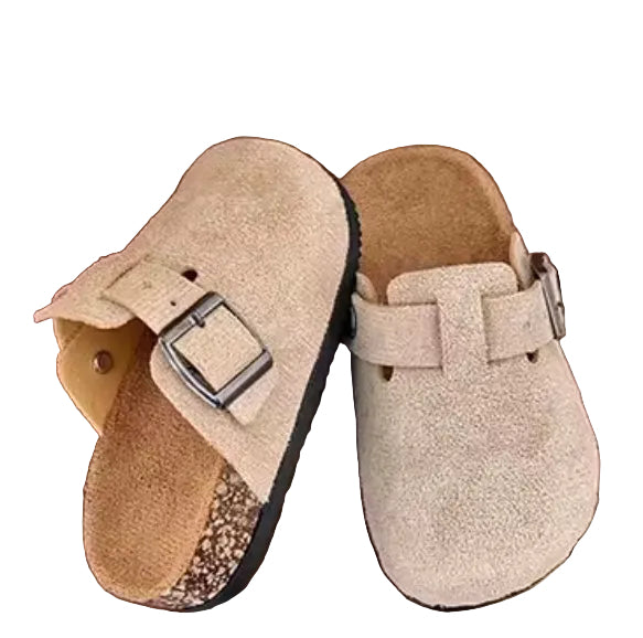 Pair of beige slippers with a buckle on a wooden surface.