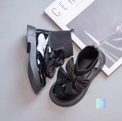 Black shoes with large bows on a light gray surface