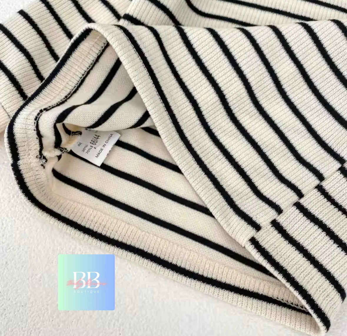 Close-up of a black and white striped sweater with a brand tag, on a light background.