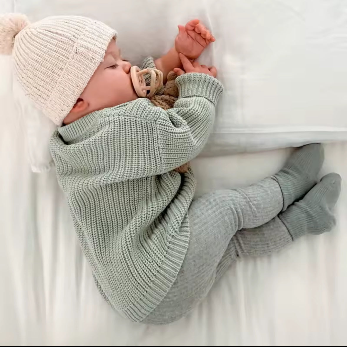 Baby wrapped in a green blanket and wearing a white knit hat on a white surface