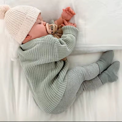 Baby wrapped in a green blanket and wearing a white knit hat on a white surface