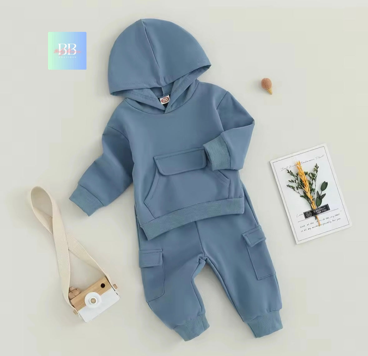 Blue baby hoodie and pants set on a light gray background with a camera and card.