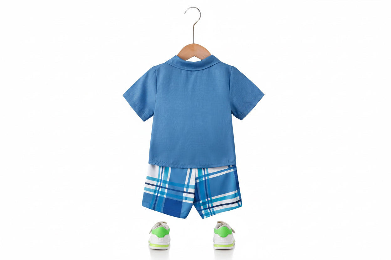 Blue children's outfit with plaid shorts on a hanger against a white wall.