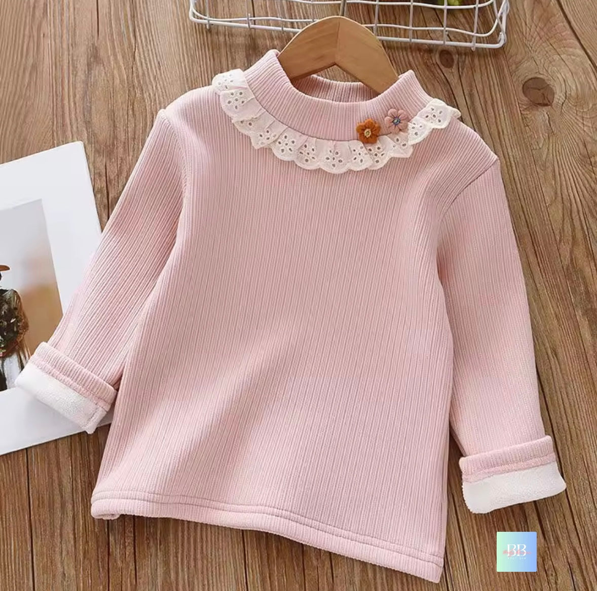 Pink ribbed sweater with lace collar on a wooden surface
