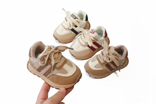 Pair of children's sneakers on a glass surface with a hand holding one shoe.