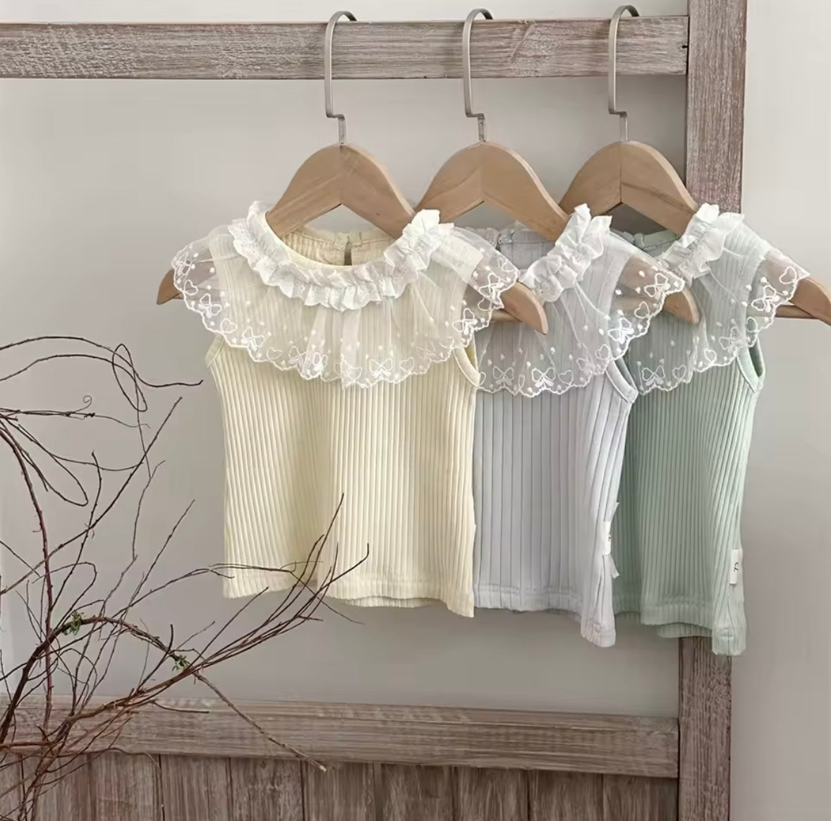 Three baby dresses with lace collars on wooden hangers against a neutral background.