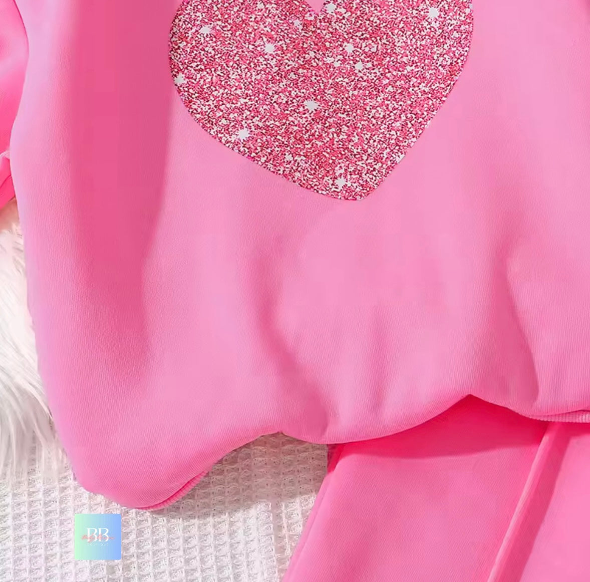Close-up of a pink garment with a glittery heart design on a textured white background.