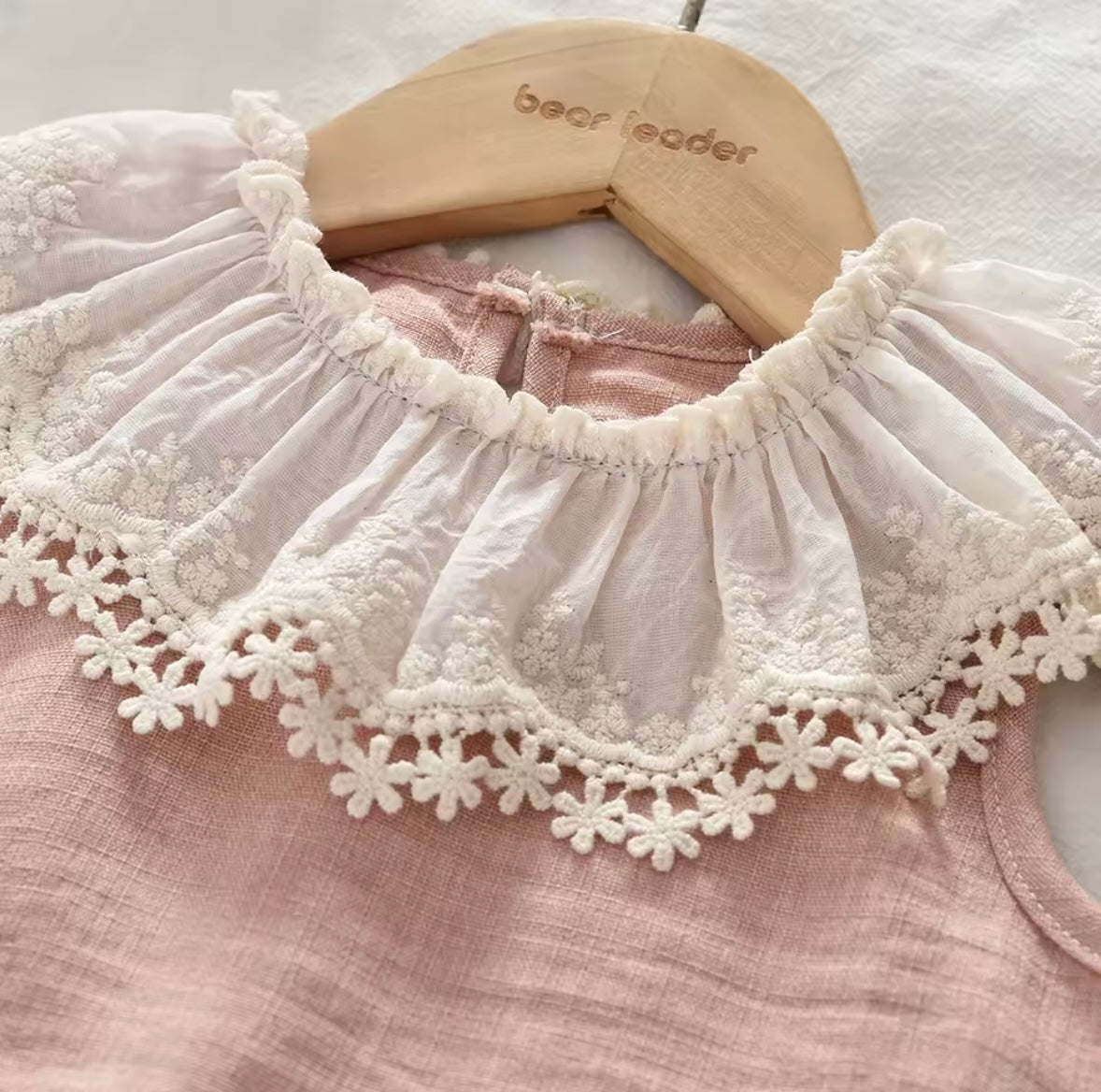 White lace collar on a pink garment with 'bear leader' hanger in the background