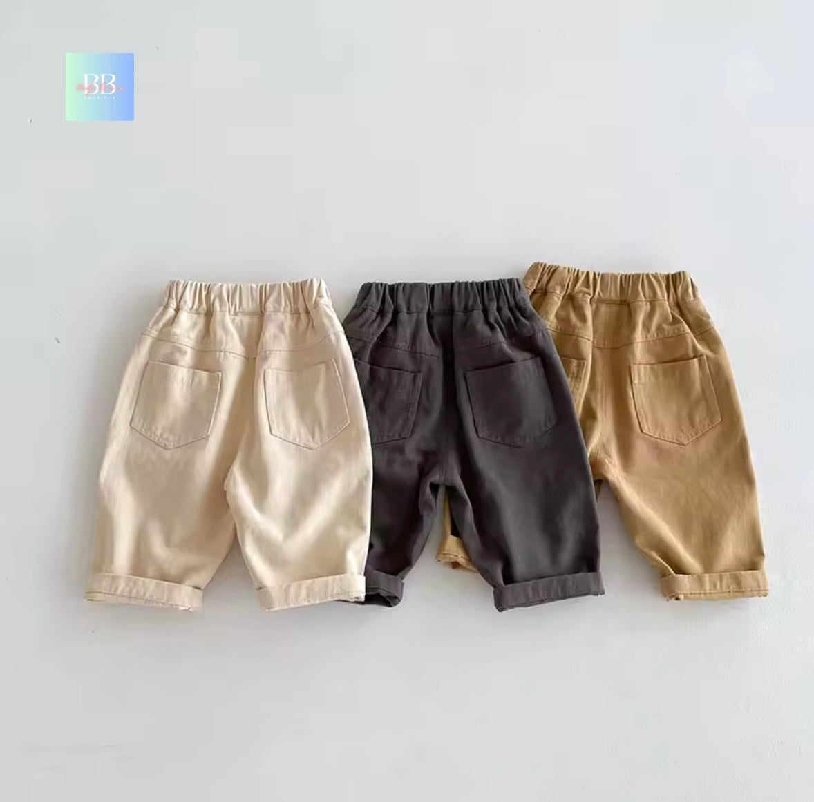 Three pairs of children's pants in beige, black, and brown on a light gray background.