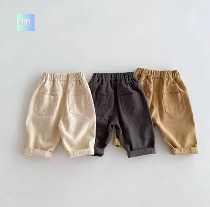 Three pairs of children's pants in beige, black, and brown on a light gray background.