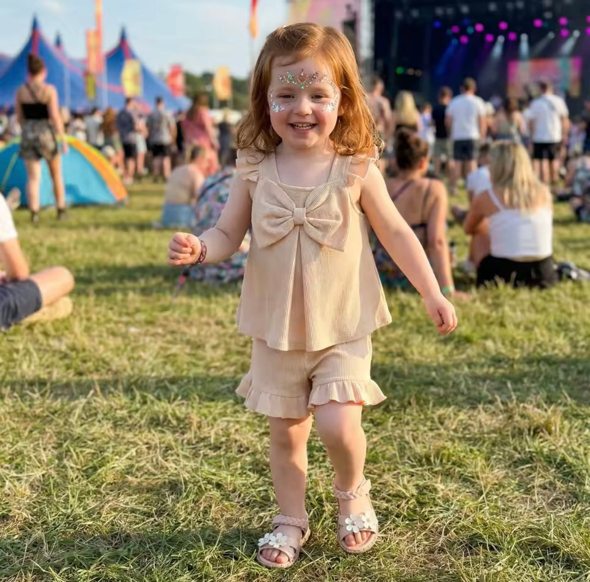 Young girl in a beige outfit with a bow at a music festival.
