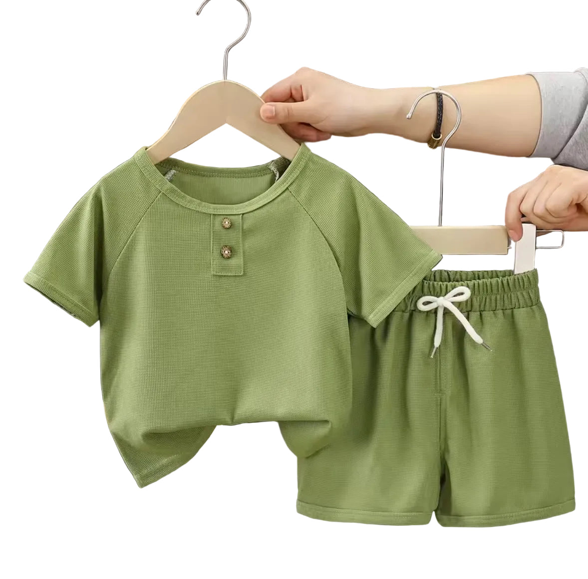 Green children's outfit with shirt and shorts on a hanger against a dark curtain background.
