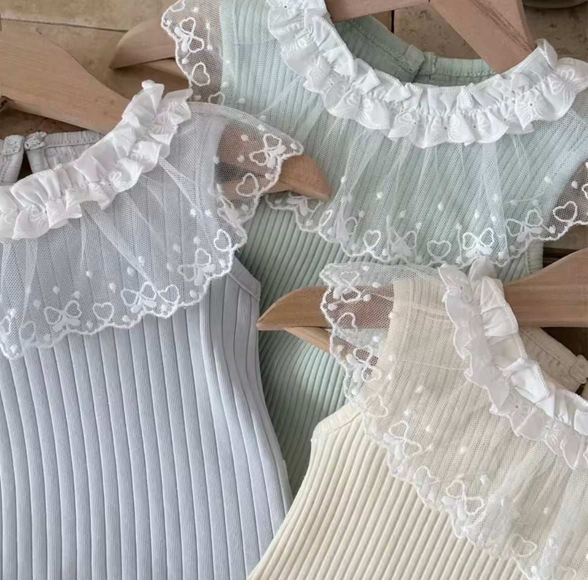 Three ribbed tank tops with lace trim on a wooden surface.