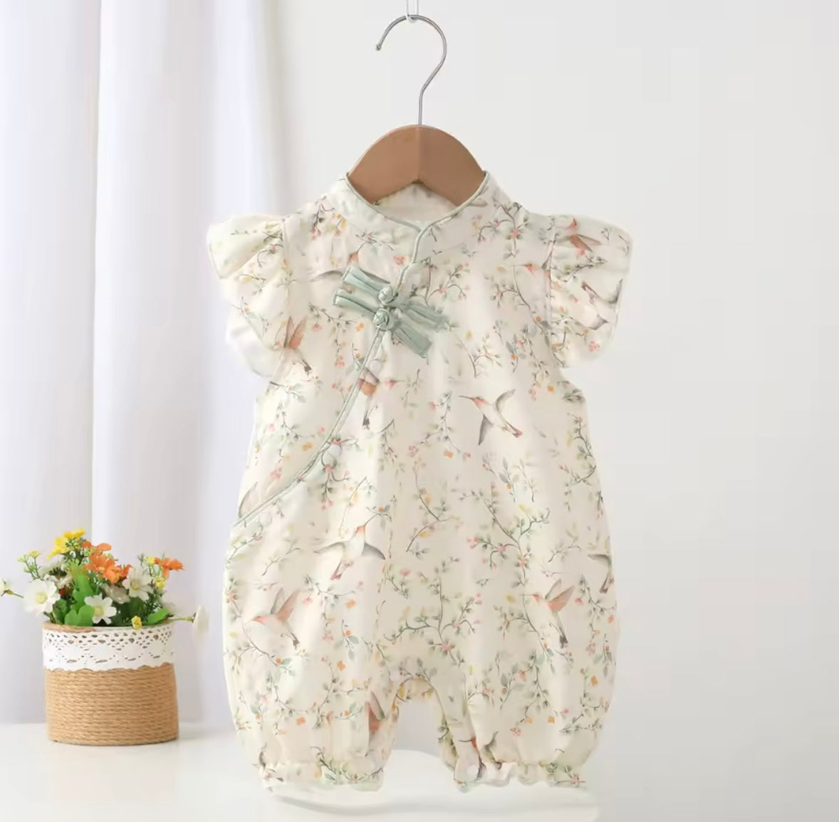 Floral baby romper on a hanger against a white background