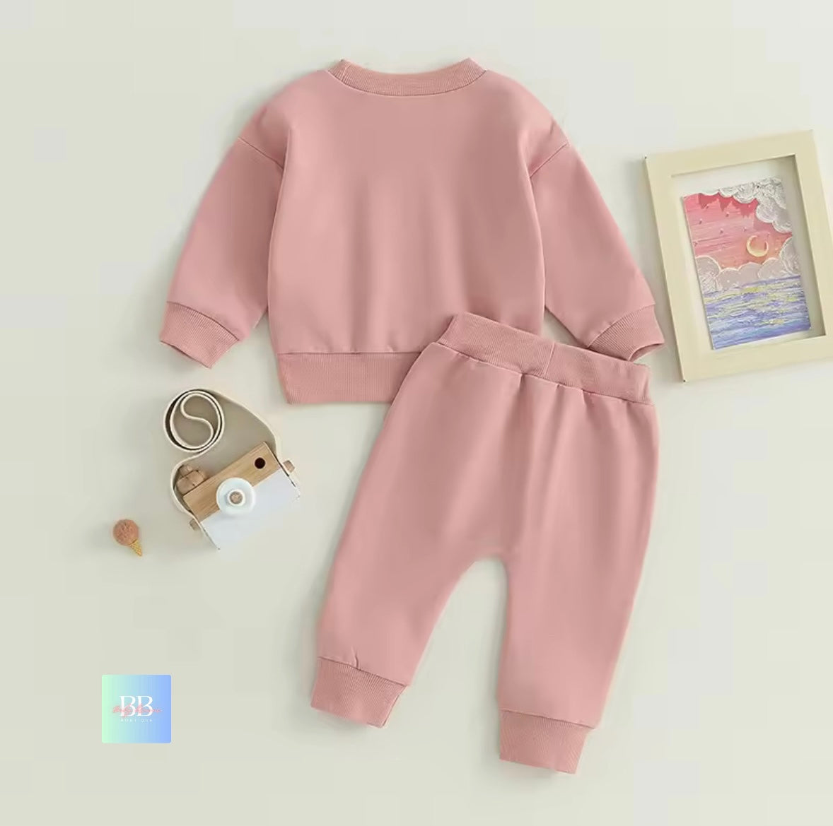 Pink baby outfit with matching headband on a light beige background