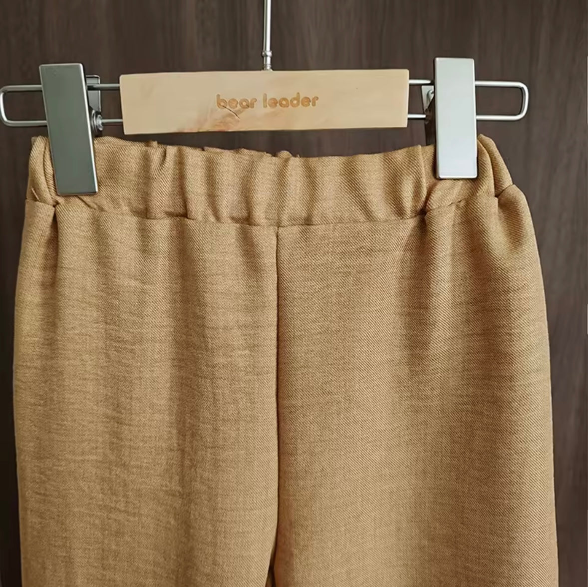 Beige pants on a hanger with 'bear leader' brand tag against a dark background