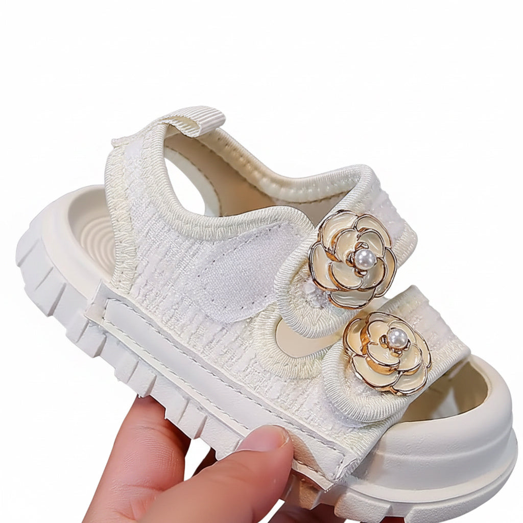 White children's shoe with floral decorations held by a hand against a neutral background