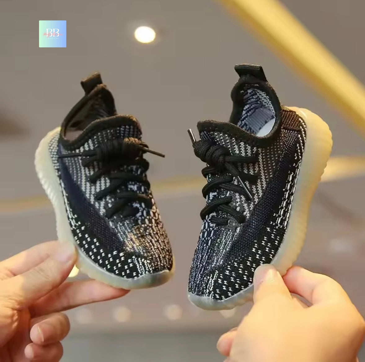 Black and white baby shoes held by two hands against a blurred background