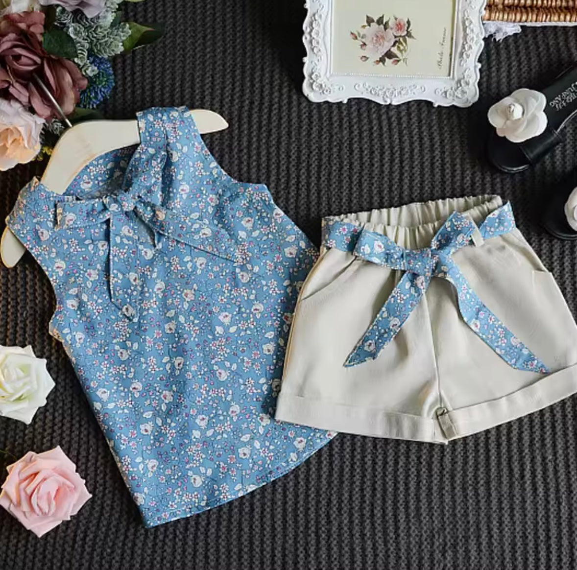Blue floral top and beige shorts with a bow on a textured surface with flowers and a frame.