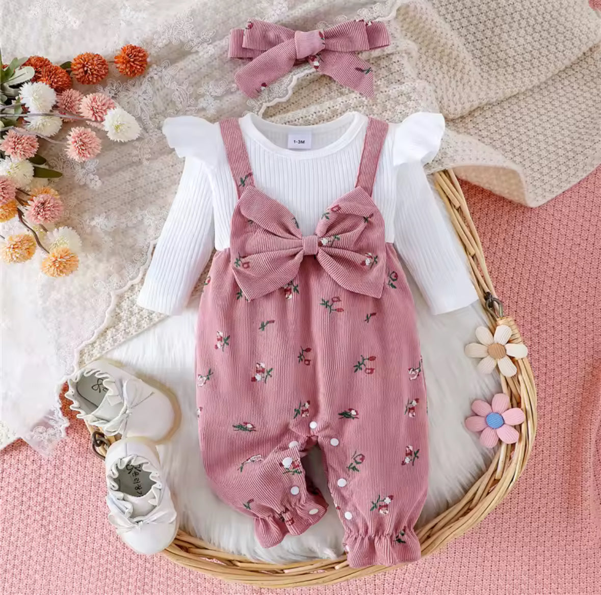 Baby outfit with pink romper, white shirt, and headband on a textured surface with flowers.