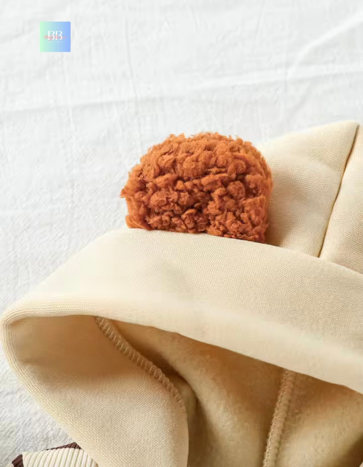 Close-up of a beige fabric with a brown pom-pom on a light gray background