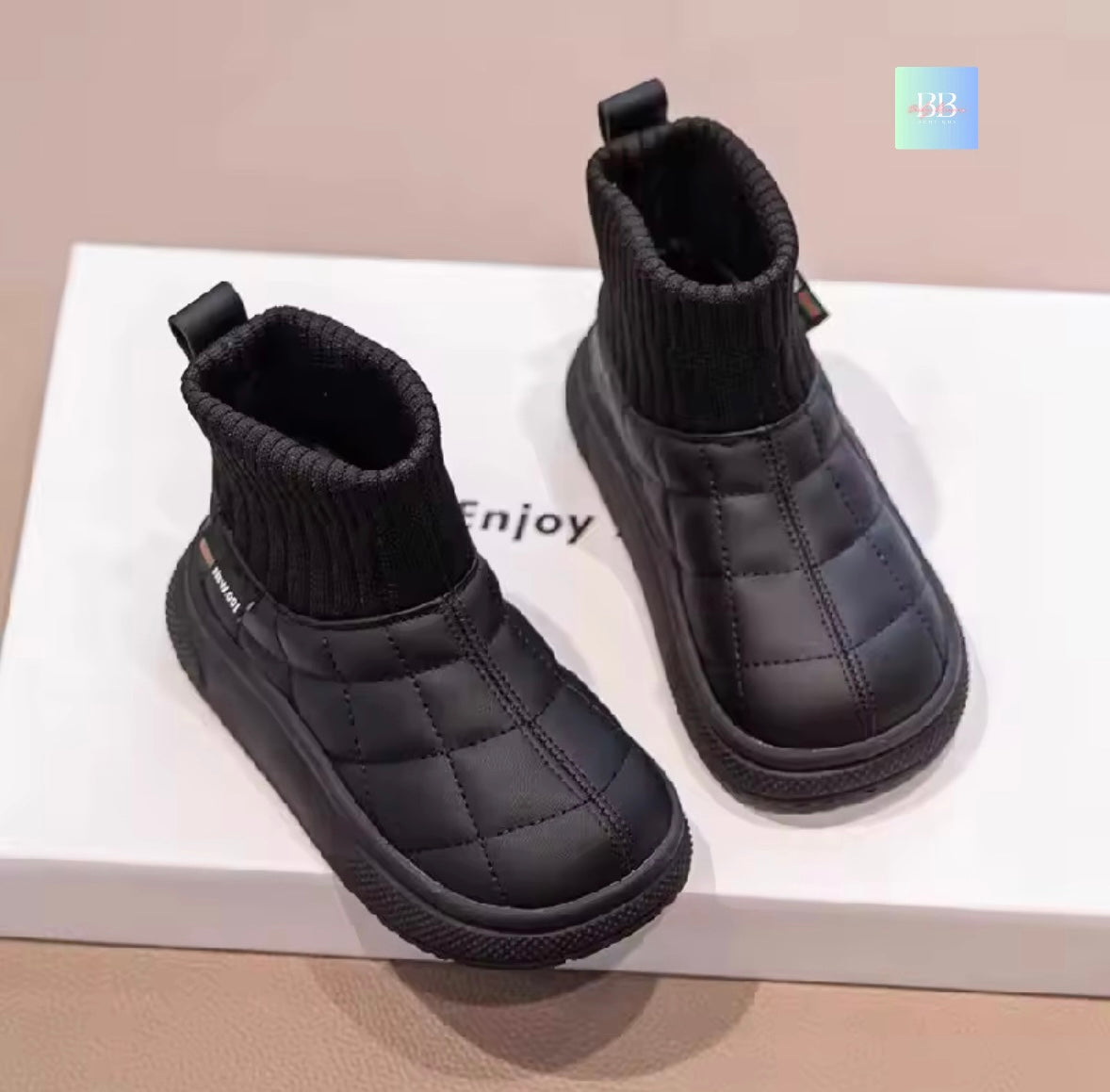 Pair of black quilted ankle boots on a white surface with 'Enjoy' text.