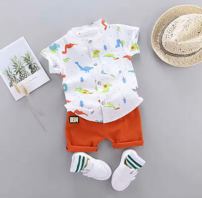 Children's outfit with dinosaur-themed shirt, orange shorts, white socks, and a hat on a gray background.