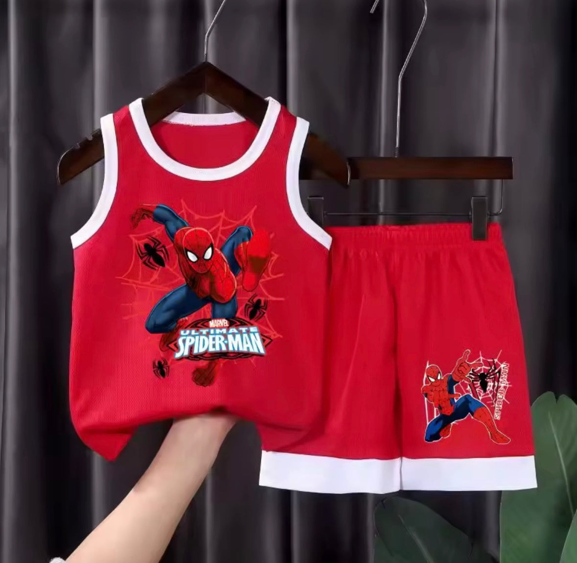 Red Spider-Man tank top and shorts set on a hanger against a dark curtain background.