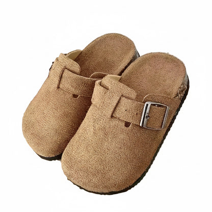 Pair of brown suede clogs with a buckle on a wooden shelf.