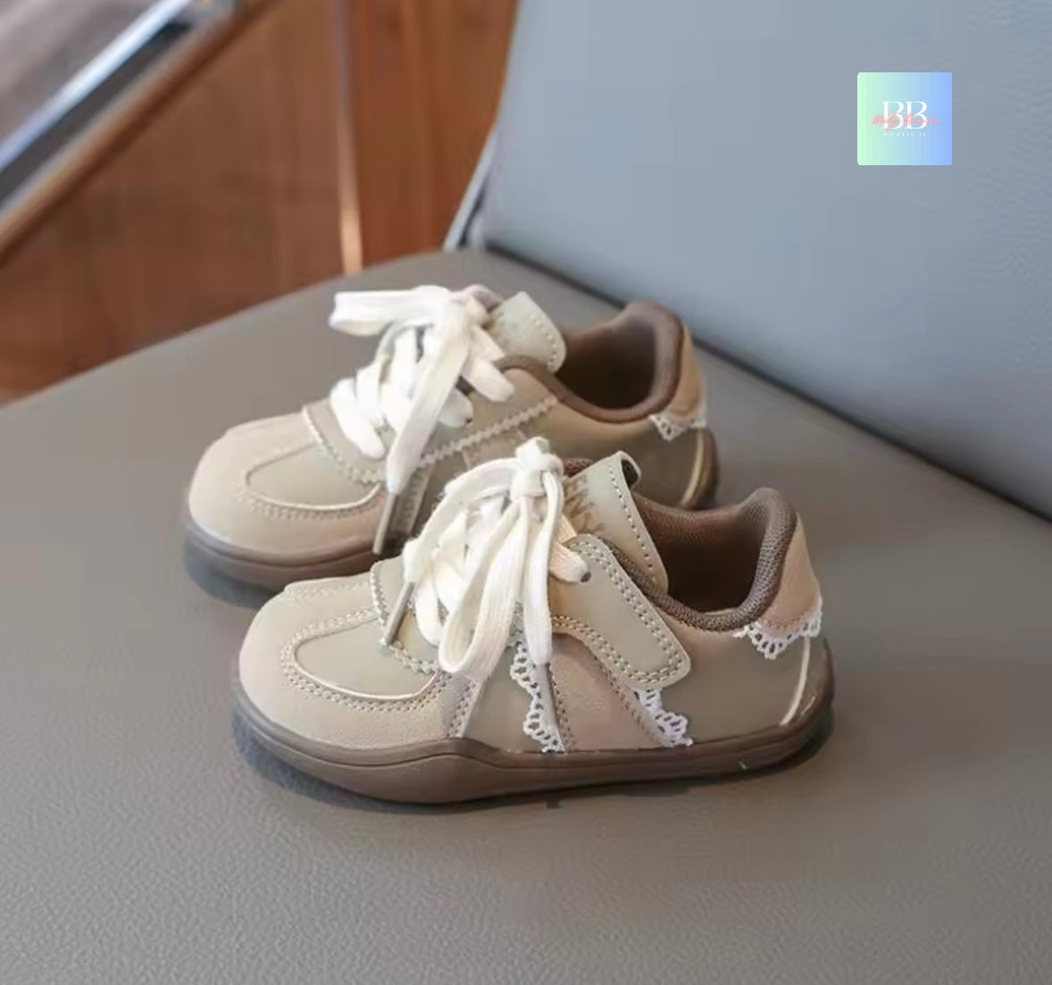 Pair of beige children's shoes with white laces on a gray surface.