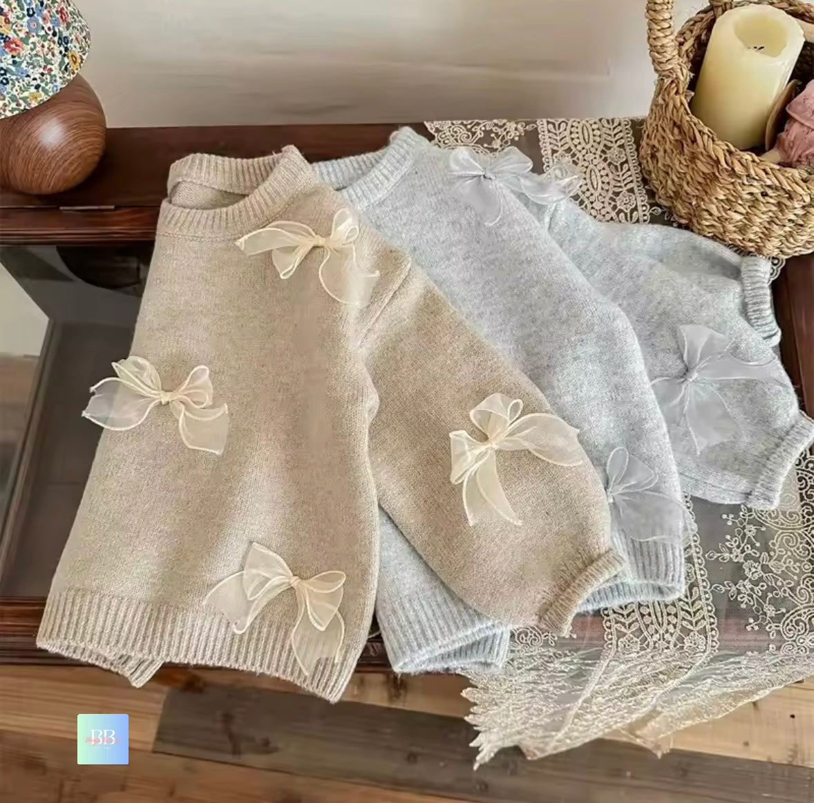 Two baby dresses with bow details on a wooden surface.