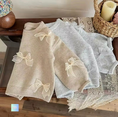 Two baby dresses with bow details on a wooden surface.