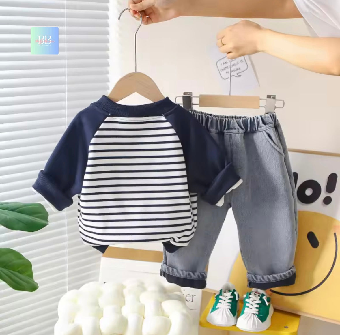 Children's outfit with striped shirt and gray pants on a hanger against a light background.